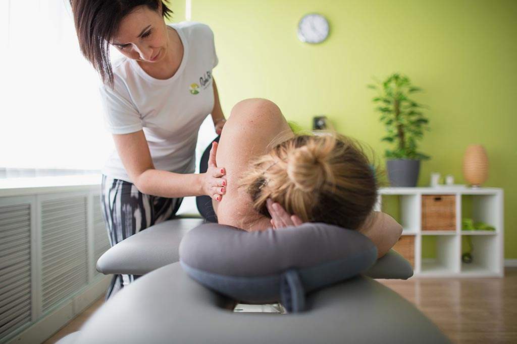 Fizjoterapeutka wykonująca masaż leczniczy pleców u pacjentki w ciąży.